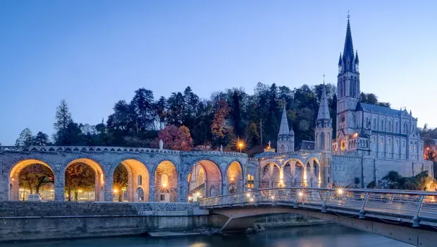 Basilica of Our Lady of Lourdes glowing at twilight, a sacred pilgrimage site radiating healing energy and faith-driven manifestation