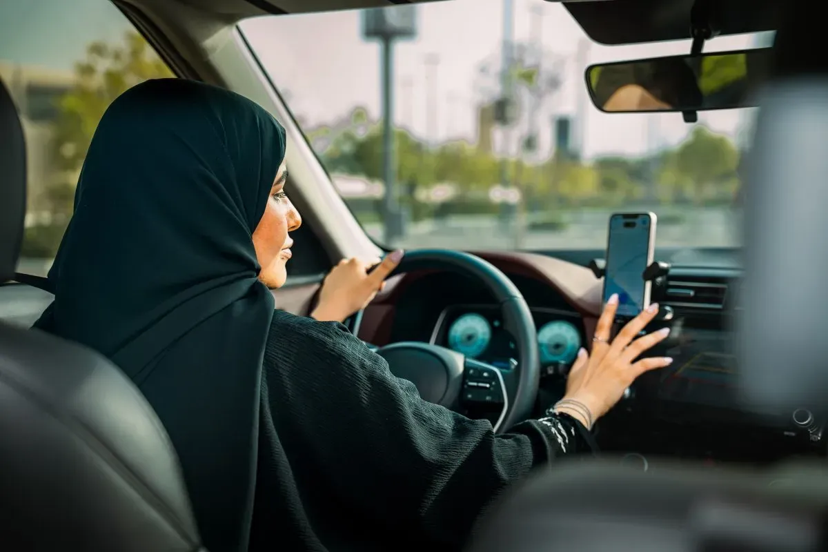 Saudi woman driving a car and using a smartphone for navigation, symbolizing empowerment and progress under Vision 2030.