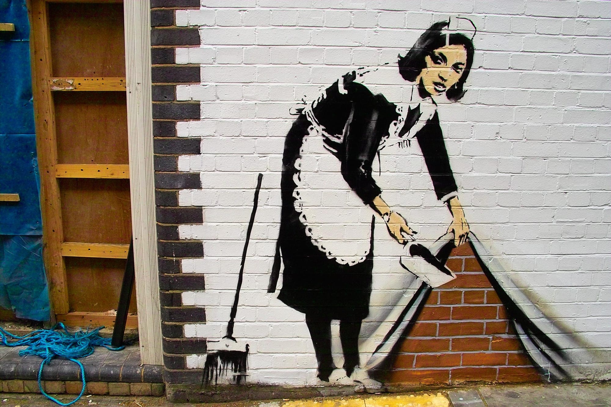 Banksy street art depicting a maid sweeping dirt behind a wall, symbolizing non-attachment, anonymity, and creative manifestation