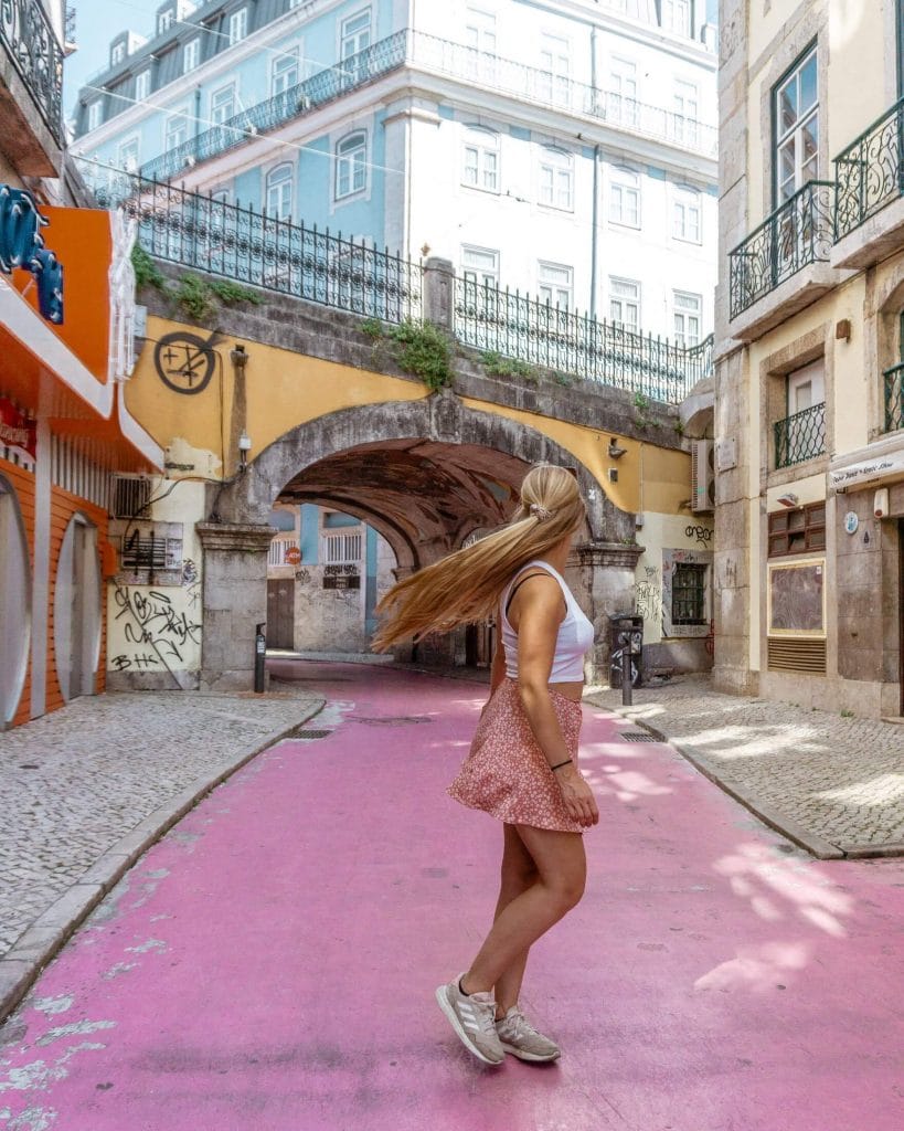 Woman walking along Pink Street in Lisbon surrounded by pastel buildings