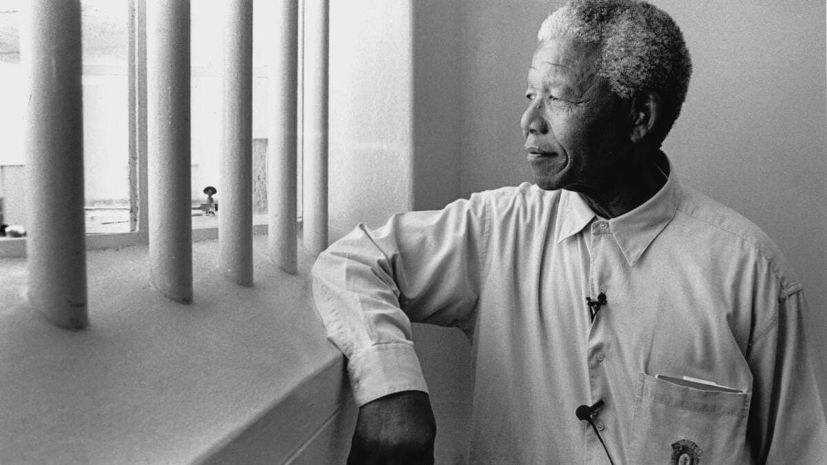 Nelson Mandela standing by a prison window on Robben Island, reflecting on freedom beyond confinement