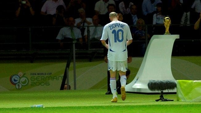 Zinedine Zidane walking off the pitch past the World Cup trophy during the 2006 final, symbolizing a moment of lost presence and human vulnerability.