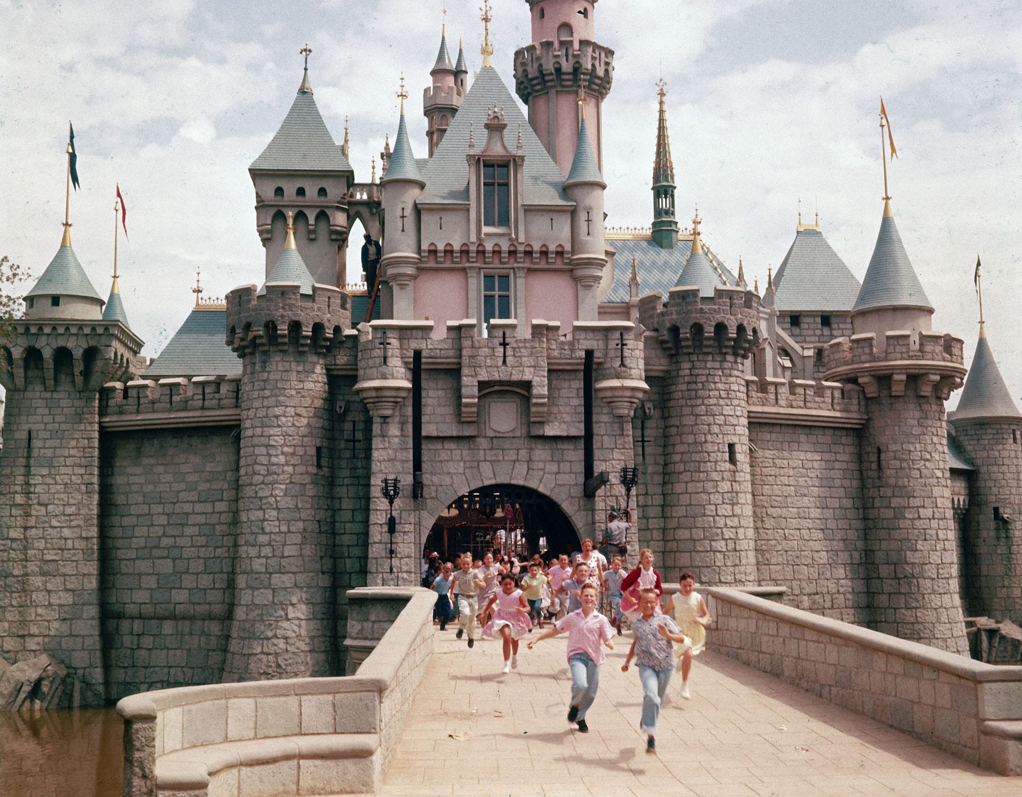 Children running across the bridge beneath Sleeping Beauty Castle at Disneyland on opening day in 1955