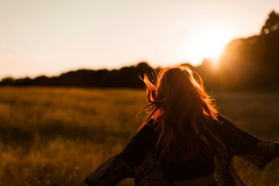 Woman running through a golden field at sunset with open arms—visualization manifestation method in action, aligned energy and joy
