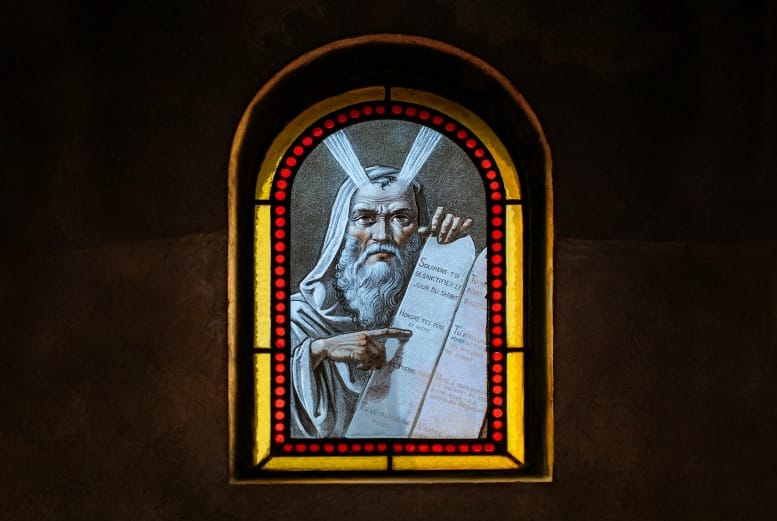 Stained glass of Moses pointing to scripture with 'I AM THAT I AM' — biblical imagery for the Moses Code and divine manifestation