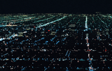 Endless illuminated city grid at night showing accelerated motion, systemic repetition, and the loss of human-scale coherence.